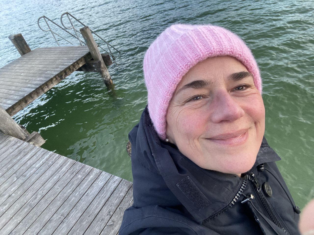 Sabine Beck draußen in der Natur am See mit rosa Mütze.